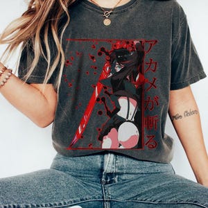 May include: Dark grey t-shirt featuring a red and black anime graphic. The graphic includes a character with a sword and Japanese text. The shirt is a relaxed fit and has short sleeves.