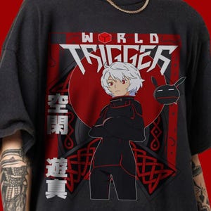 May include: Black t-shirt with a red and white graphic design featuring a character from the anime "World Trigger". The graphic includes the text "WORLD TRIGGER" in a stylized font and Japanese characters.