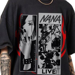 May include: Black graphic t-shirt featuring manga-style illustrations. The design includes a woman smoking, the word "NANA", and band members playing instruments. Red flame-like shapes frame the design. Japanese text is also present.