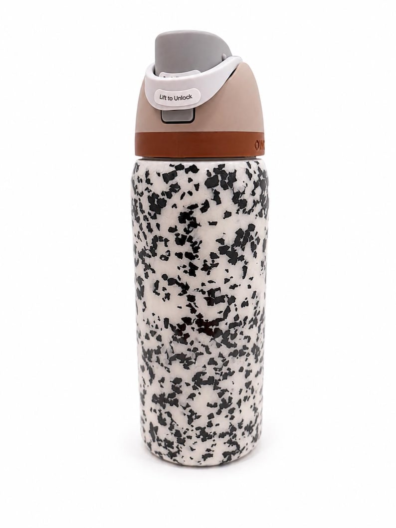 Pu&ograve; includere: Una borraccia riutilizzabile con un motivo maculato bianco e nero. Il coperchio &egrave; beige e grigio con una fascia marrone. Sul coperchio c'&egrave; la scritta "Lift to Unlock".