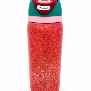 May include: A cylindrical water bottle with a vibrant red glitter finish. The lid features a teal band, a light pink ring, and a red top section. White labels on the lid display the text Push Button and Lift to Unlock in black font.