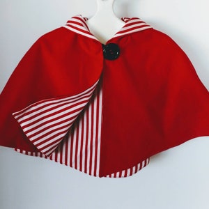 May include: Red cape with a white and red striped lining. The cape has a black button closure.