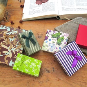 May include: A collection of six square and rectangular gift boxes featuring various designs including a brown floral pattern, a green polka dot box with a dark green bow, a lime green floral box, a butterfly print, purple stripes with a purple bow, and a red box with two white hearts.