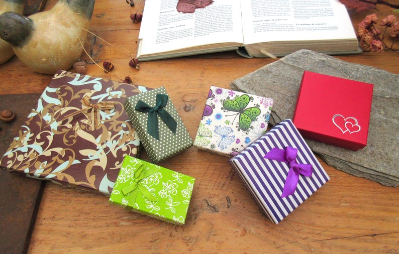 May include: A collection of six square and rectangular gift boxes featuring various designs including a brown floral pattern, a green polka dot box with a dark green bow, a lime green floral box, a butterfly print, purple stripes with a purple bow, and a red box with two white hearts.