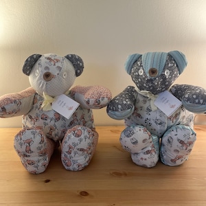 May include: Two handmade fabric teddy bears. One bear has a light background with a fox pattern and pink accents. The other bear has a dark background with a floral pattern and blue accents. Each bear has a tag.