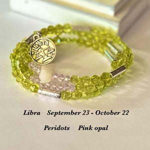 May include: A triple-wrap bracelet with green and pink beads, a silver charm with the Libra zodiac symbol, and the text "Libra September 23 - October 22 Peridots Pink opal".