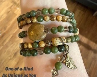 May include: Several beaded bracelets in shades of green, brown, and clear. A large, round, tan stone is a feature of one bracelet. A gold-coloured feather charm hangs from one bracelet. The text "One-of-a-Kind As Unique as You" is visible.
