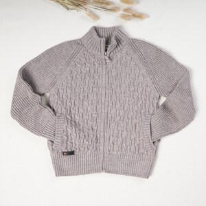 Peut inclure: Un pull gris à fermeture éclair en tricot avec un motif en câble.