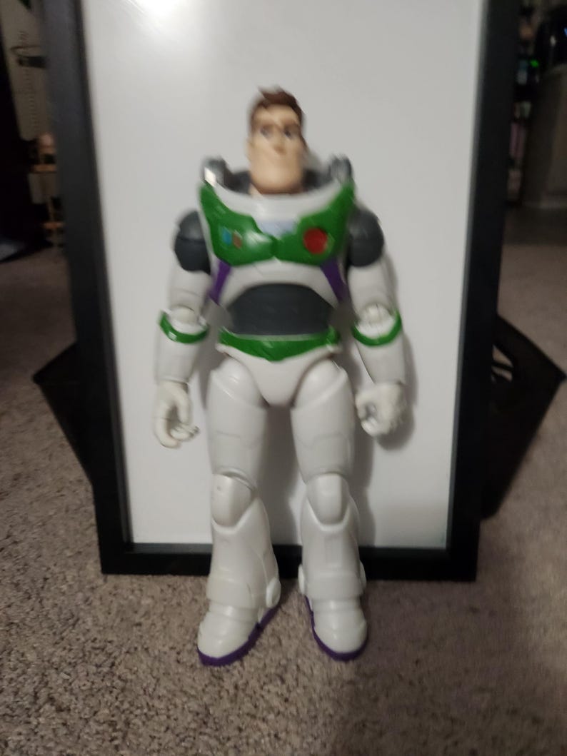 May include: A Buzz Lightyear action figure, featuring a white spacesuit with green and purple accents. The toy has a detailed face and is standing upright. The figure's boots have purple soles.