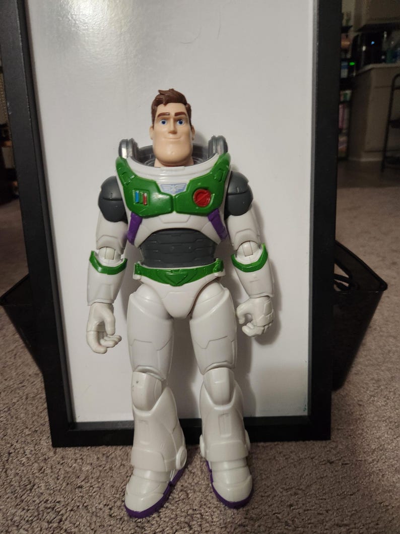 May include: A Buzz Lightyear action figure, standing upright. The figure is predominantly white with green, purple, and black accents. It features a helmet, chest armor, and boots. The figure is a toy from the Toy Story franchise.