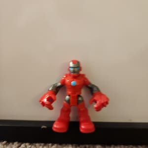 May include: A red Iron Man action figure with a blue and silver helmet and red boots. The figure has gray arms and large red hands. A blue circle is on the chest.