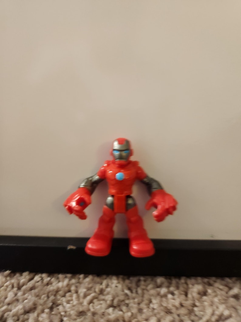 May include: A red Iron Man action figure with a blue and silver helmet and red boots. The figure has gray arms and large red hands. A blue circle is on the chest.