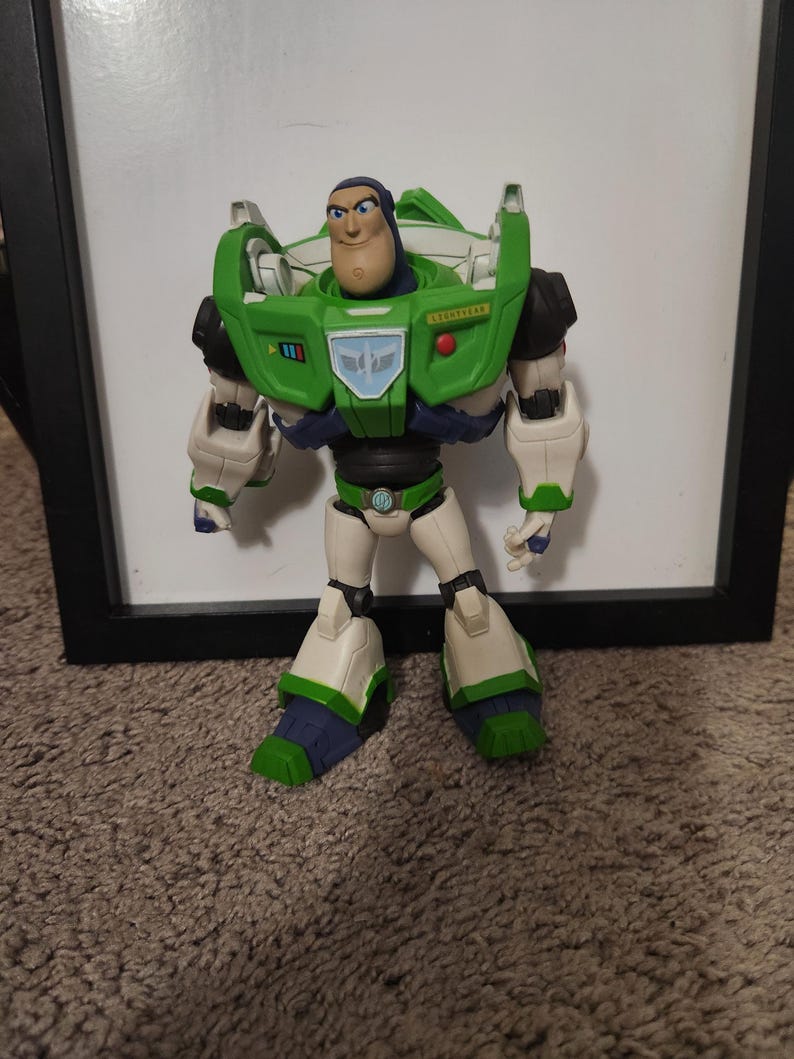 May include: A Buzz Lightyear action figure, featuring a green and white spacesuit with blue and black accents. The figure has a determined expression and is posed in a standing position. The toy is set against a neutral background.