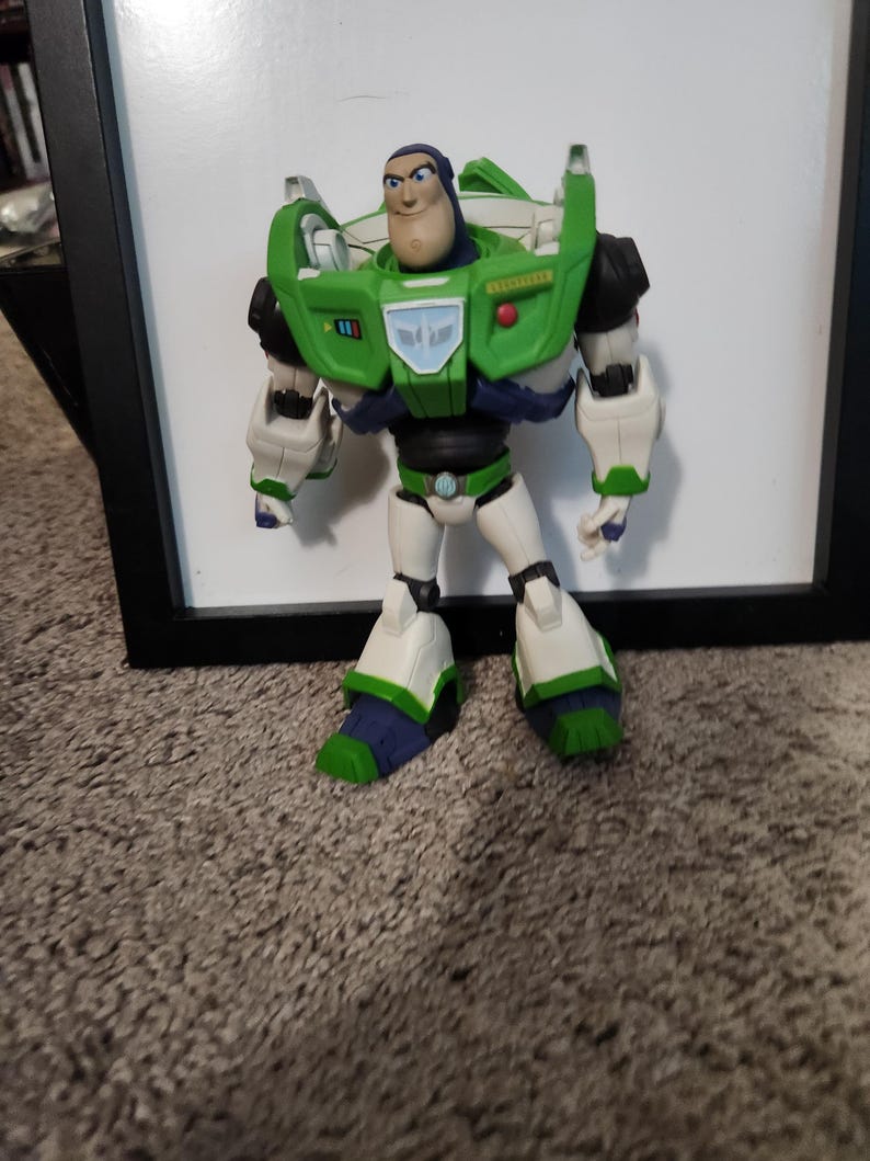 May include: A Buzz Lightyear action figure, featuring a green and white spacesuit with black accents. The figure has a determined expression and is standing in front of a white background.