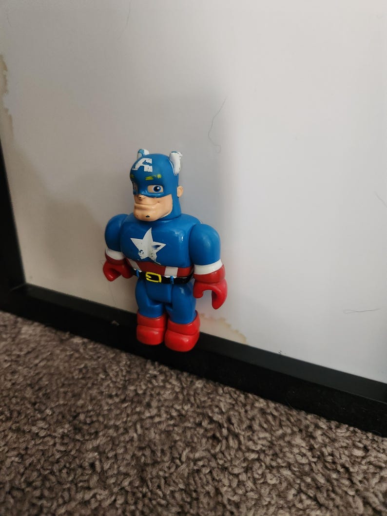 May include: A Captain America action figure in a stylized design. The figure is primarily blue with red gloves and boots. A white star is on the chest. The figure is standing in front of a white background.