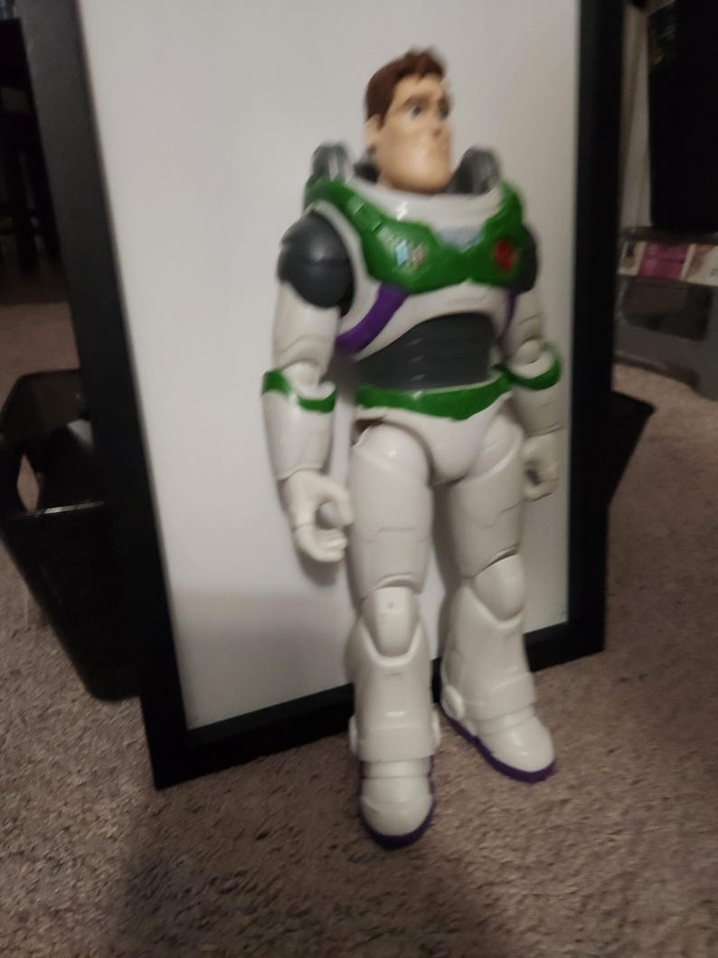May include: A Buzz Lightyear action figure, featuring a white and green spacesuit with purple accents. The figure has a detailed face and is standing upright. The toy is a collectible item.