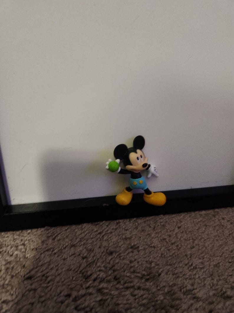 Op de afbeelding: Een Mickey Mouse-beeldje in een staande pose, met een groene bal. Het figuur heeft zwarte oren, een zwart gezicht en een witte handschoen. Mickey draagt gele schoenen, een blauwe korte broek met gele knopen en een zwart-wit shirt.