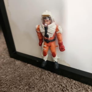 May include: A small astronaut action figure in an orange and white spacesuit. The figure has a clear helmet, red gloves, and black boots. The figure is standing in front of a white background.