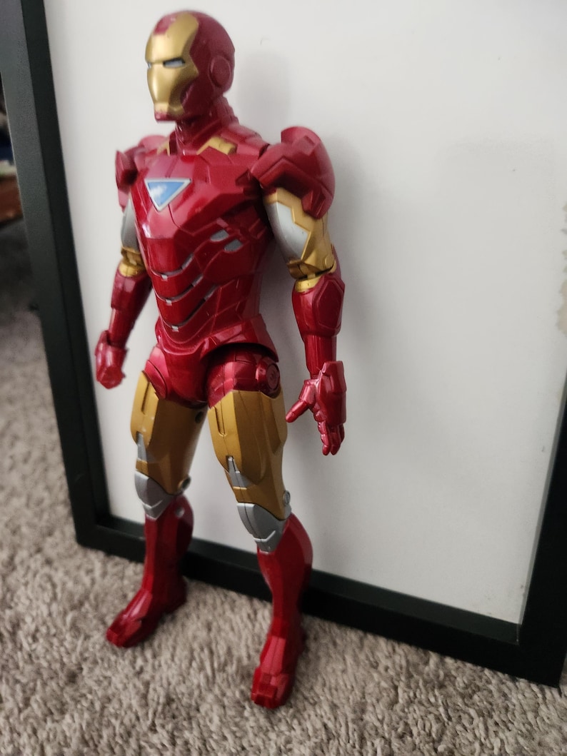 May include: An Iron Man action figure featuring a metallic red and gold suit with silver accents. The character has a triangular light blue chest piece, a full face mask, and articulated limbs, standing in a vertical position with a detailed armor design.