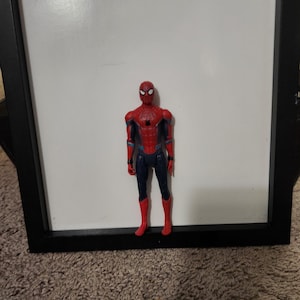 Op de afbeelding: Een rood, blauw en zwart Spider-Man actiefiguur. Het figuur staat voor een witte achtergrond. Het figuur draagt een rood en zwart pak met een spinnenwebontwerp.