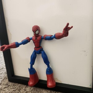 May include: A red and blue Spider-Man action figure with a web pattern on the head and chest. The figure has articulated joints at the shoulders, elbows, hips, and knees, with one hand posed in a web-shooting gesture and the other hand open.