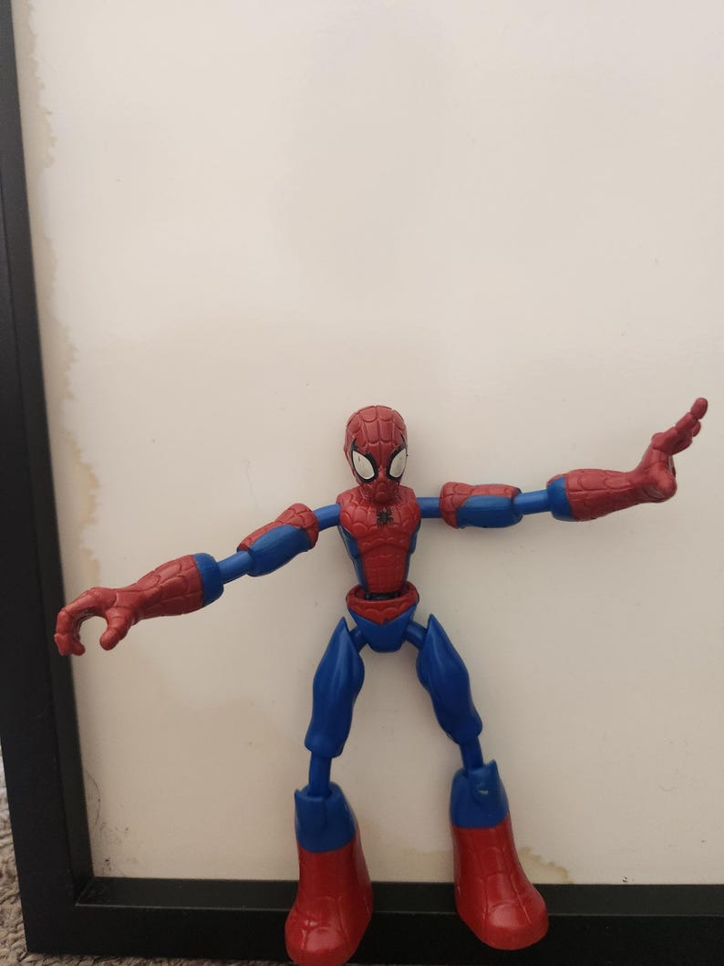 May include: A red and blue plastic action figure of a superhero character with a web pattern on the head and chest. The figure has articulated joints at the shoulders, elbows, hips, and knees, and is posed with arms extended outward to the sides.