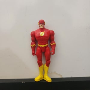 May include: A red action figure of The Flash with yellow boots, a yellow lightning bolt emblem on the chest, and yellow lightning bolt accents on the forearms and waist. The figure has a smooth red mask covering the head with yellow lightning details.