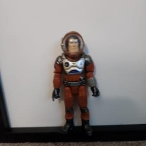 K&ouml;nnte beinhalten: Spielzeug-Astronautenfigur in einem rot-silbernen Raumanzug mit transparentem Helm. Die Figur hat schwarze Stiefel und Handschuhe. Der Astronaut steht vor einem wei&szlig;en Hintergrund.