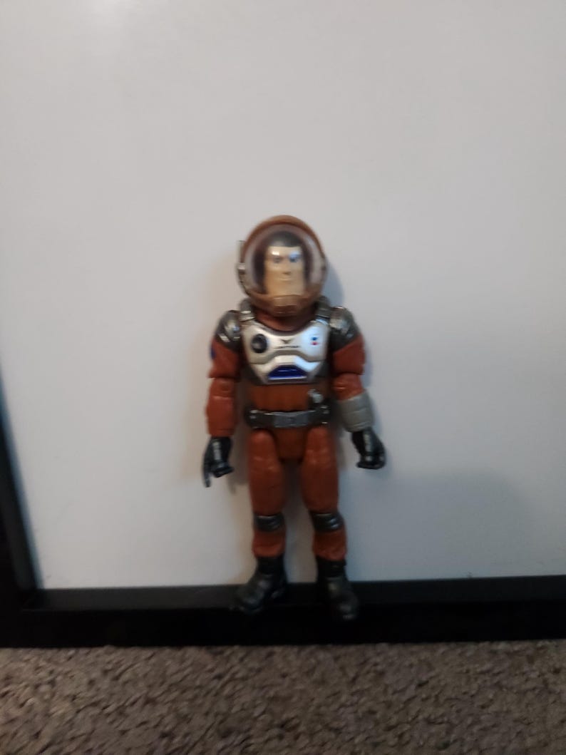 K&ouml;nnte beinhalten: Spielzeug-Astronautenfigur in einem rot-silbernen Raumanzug mit transparentem Helm. Die Figur hat schwarze Stiefel und Handschuhe. Der Astronaut steht vor einem wei&szlig;en Hintergrund.
