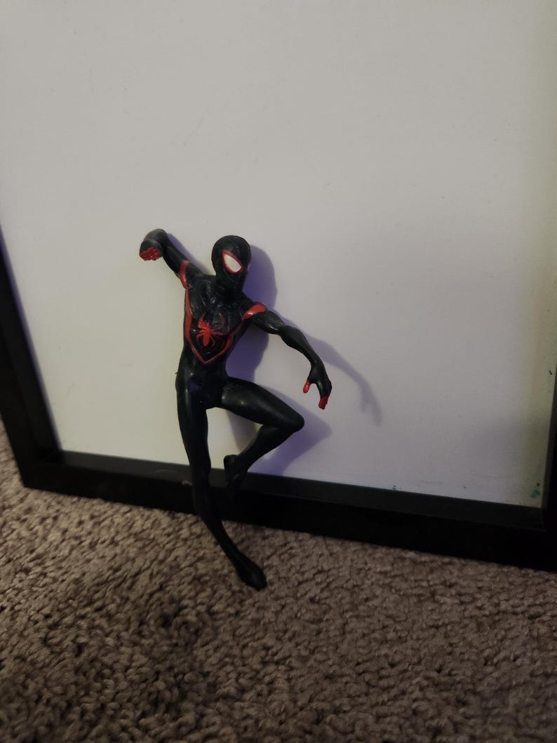 Puede incluir: Figura de acci&oacute;n de Spider-Man negro y rojo en una pose din&aacute;mica. La figura tiene un emblema de ara&ntilde;a roja en el pecho y detalles rojos en brazos y manos. Fondo blanco.
