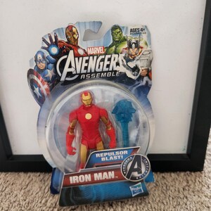 May include: A plastic action figure of Iron Man from the Marvel Avengers Assemble series. The figure is red and gold with a repulsor blast effect. The figure is packaged in a plastic blister pack with a blue and white background. The packaging features the Marvel Avengers Assemble logo and the words "Repulsor Blast!" and "Iron Man".