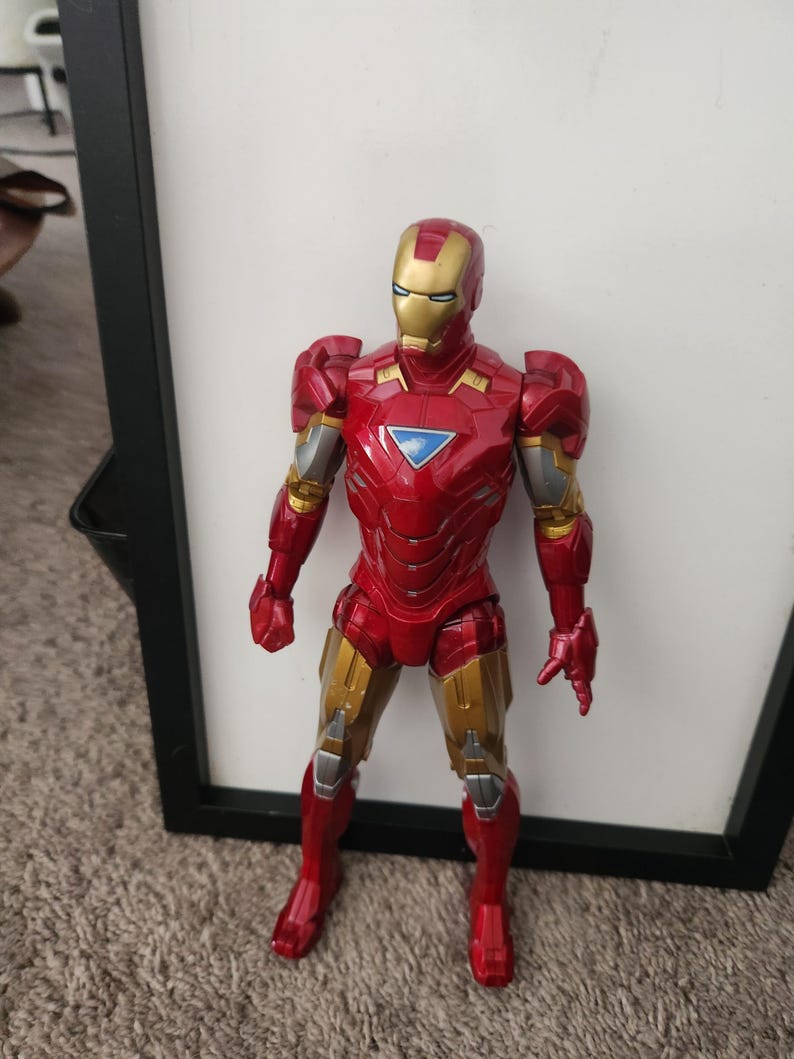 May include: An Iron Man action figure featuring a metallic red and gold suit with a triangular blue chest piece. The character is depicted in a standing position with articulated limbs, a detailed helmet, and silver accents on the arms and legs.