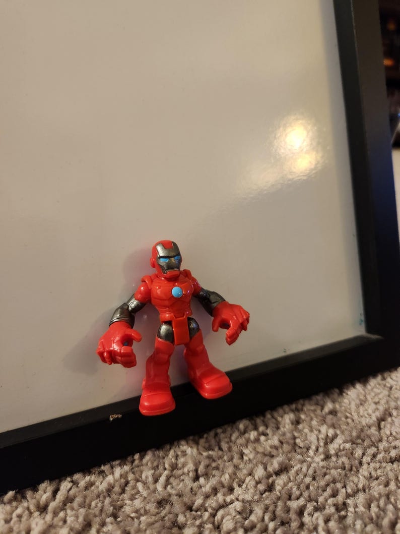 May include: A red and silver Iron Man action figure. The toy has a red helmet with a silver faceplate, red body, and silver arms. A blue circle is on the chest. The figure is standing on a carpeted surface.