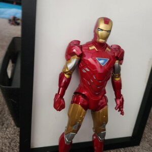 May include: An Iron Man action figure featuring a metallic red and gold suit with silver accents. The figure has a triangular blue arc reactor on the chest, a gold faceplate with white eye slits, and articulated joints throughout the body.