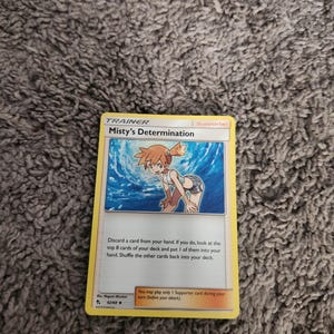 May include: A yellow Trainer card featuring "Misty's Determination" with an illustration of a character in a blue and white outfit. The card text describes game instructions. The card is a "Supporter" card.