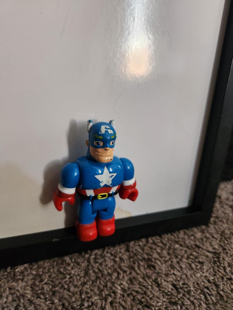May include: A Captain America action figure. The figure is primarily blue with red gloves and boots. The chest features a white star on a white background. The figure has a blue mask with a white "A" on the forehead.