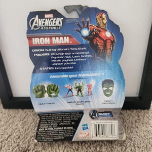 May include: A plastic action figure packaging featuring Iron Man from the Marvel Avengers Assemble series. The packaging is blue and red with a picture of Iron Man in his red and gold suit. The back of the packaging shows the different parts of the action figure, including Hulk's hands, Captain America's figure, and Hulk's mask.