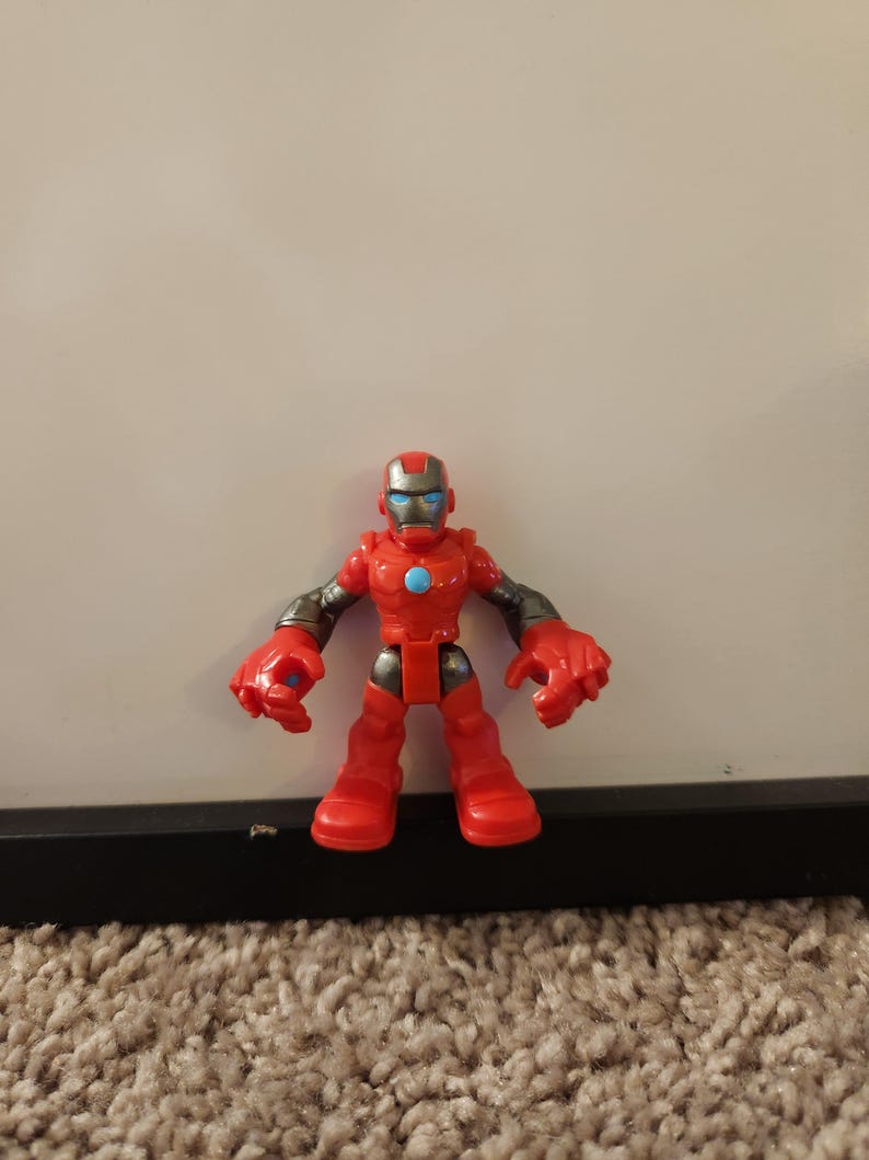 May include: A red and silver Iron Man action figure. The toy has a red body, legs, and hands, with silver arms and a helmet. The figure has a blue circle on its chest and blue eyes.