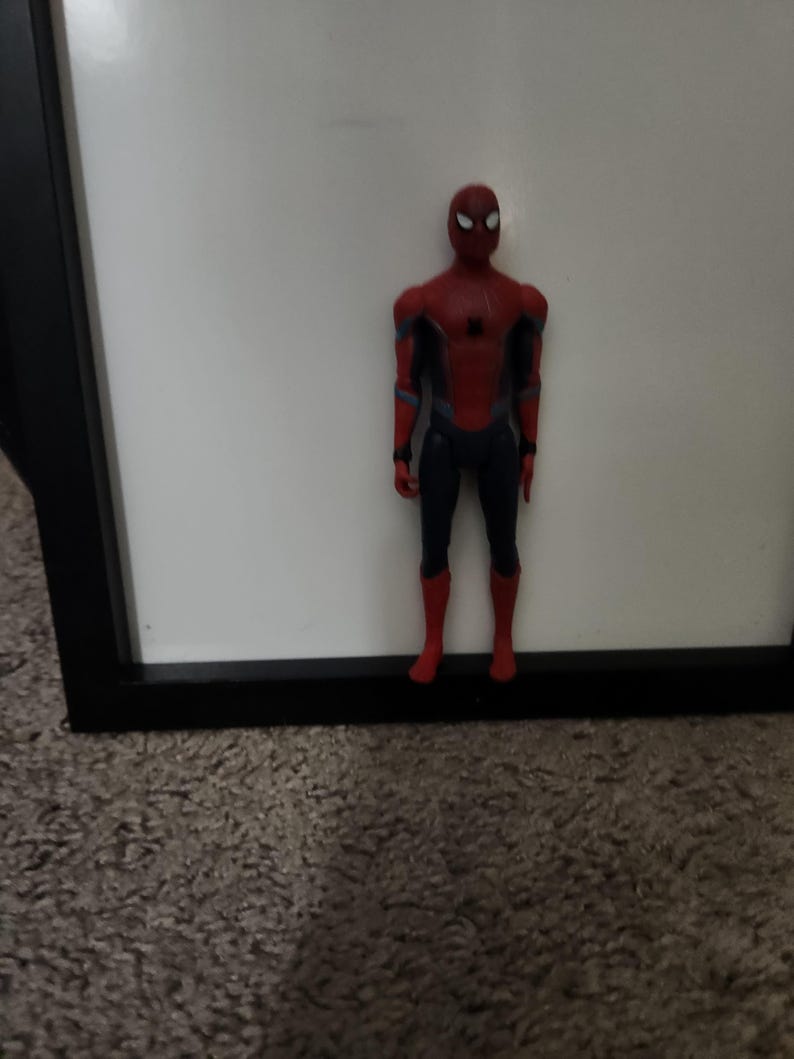 Op de afbeelding: Een Spider-Man actiefiguur, met een rood en zwart pak en een gedetailleerd masker. De figuur staat op een tapijt, met een witte achtergrond en een zwart frame. De figuur is ongeveer 15 cm hoog.