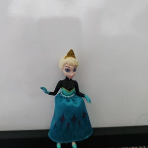 May include: A small plastic doll of a princess wearing a blue and black dress with a gold crown.