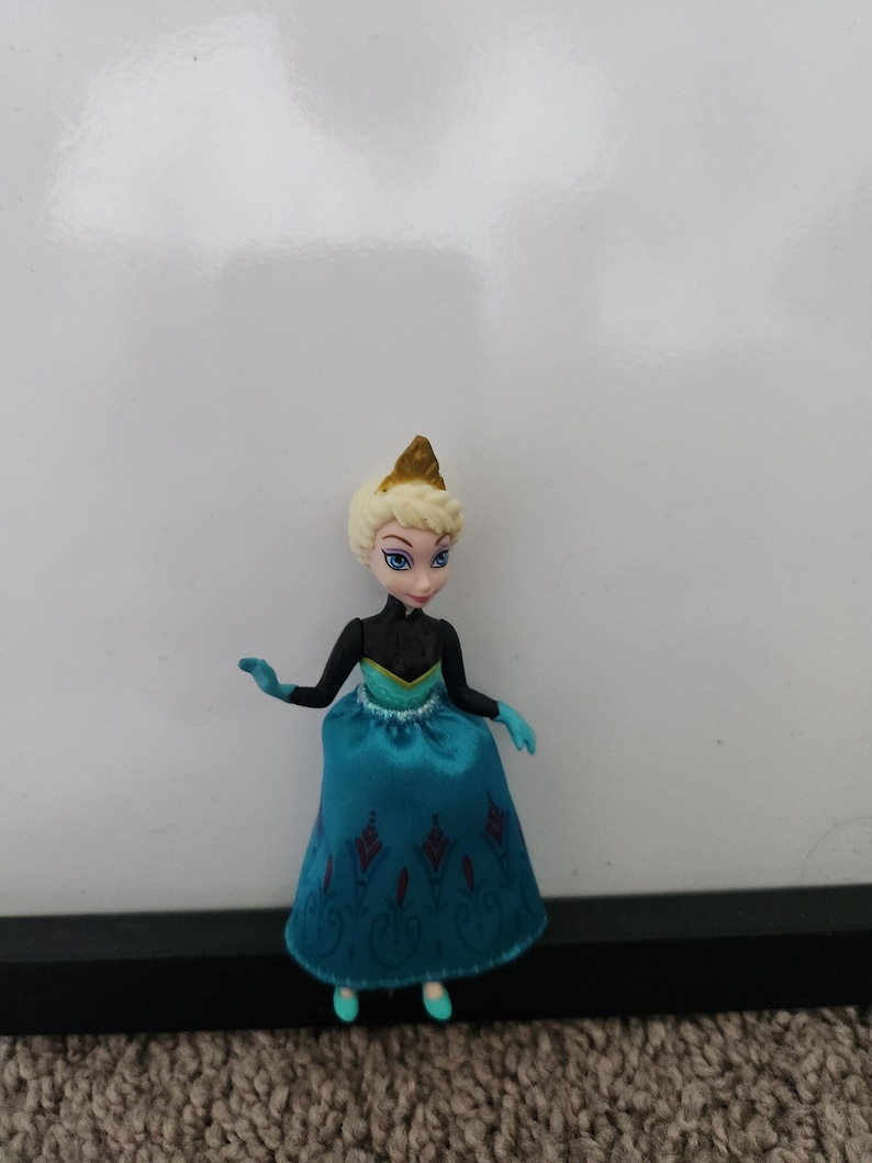 May include: A small plastic doll of a princess wearing a blue and black dress with a gold crown.