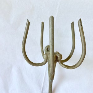 Puede incluir: Un perchero de metal plateado con cuatro brazos curvos y un soporte vertical central. Los brazos est&aacute;n espaciados uniformemente y tienen una forma redondeada, con un peque&ntilde;o elemento decorativo en la base.
