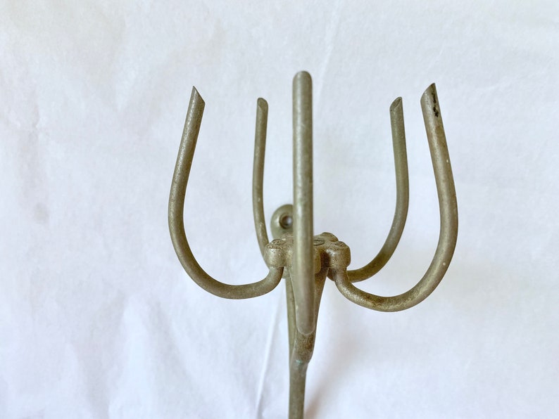 Puede incluir: Un perchero de metal plateado con cuatro brazos curvos y un soporte vertical central. Los brazos est&aacute;n espaciados uniformemente y tienen una forma redondeada, con un peque&ntilde;o elemento decorativo en la base.