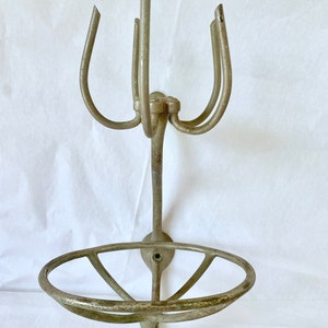 Puede incluir: Un jabonera y soporte de metal antiguo, montado en la pared. El soporte tiene una base circular con radios y un v&aacute;stago central que sostiene brazos curvos. El metal tiene un aspecto envejecido y desgastado.