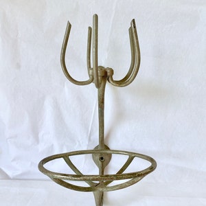Puede incluir: Un jabonera y toallero de metal antiguo montado en la pared. La jabonera tiene un dise&ntilde;o circular y abierto, y el toallero tiene tres brazos curvos. El metal tiene un aspecto envejecido.