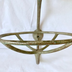 Puede incluir: Un jabonera de pared de estilo antiguo. La jabonera es de metal con un aspecto envejecido y desgastado. El soporte circular para jab&oacute;n est&aacute; sostenido por un v&aacute;stago vertical y una placa trasera decorativa, mostrando una est&eacute;tica vintage.