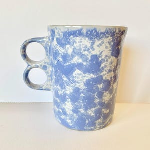 May include: A blue and white ceramic mug with a unique double handle design. The mug has a speckled glaze with a blue and white pattern.