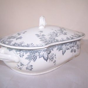 May include: White ceramic serving dish with a lid, featuring a gray and white floral pattern of leaves and berries.