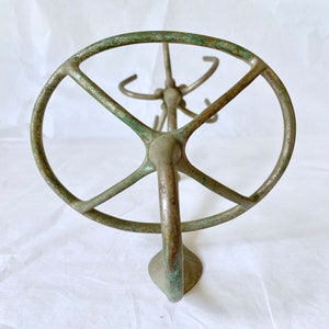 Puede incluir: Un expositor de metal de color bronce antiguo con una parte superior circular y m&uacute;ltiples ganchos. El expositor tiene un acabado de p&aacute;tina, que muestra signos de edad y uso. La base tiene forma redondeada. El expositor est&aacute; dise&ntilde;ado para contener varios art&iacute;culos.