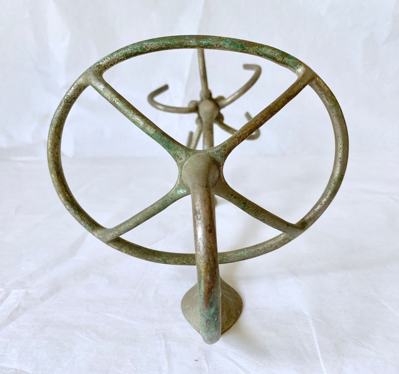 Puede incluir: Un expositor de metal de color bronce antiguo con una parte superior circular y m&uacute;ltiples ganchos. El expositor tiene un acabado de p&aacute;tina, que muestra signos de edad y uso. La base tiene forma redondeada. El expositor est&aacute; dise&ntilde;ado para contener varios art&iacute;culos.